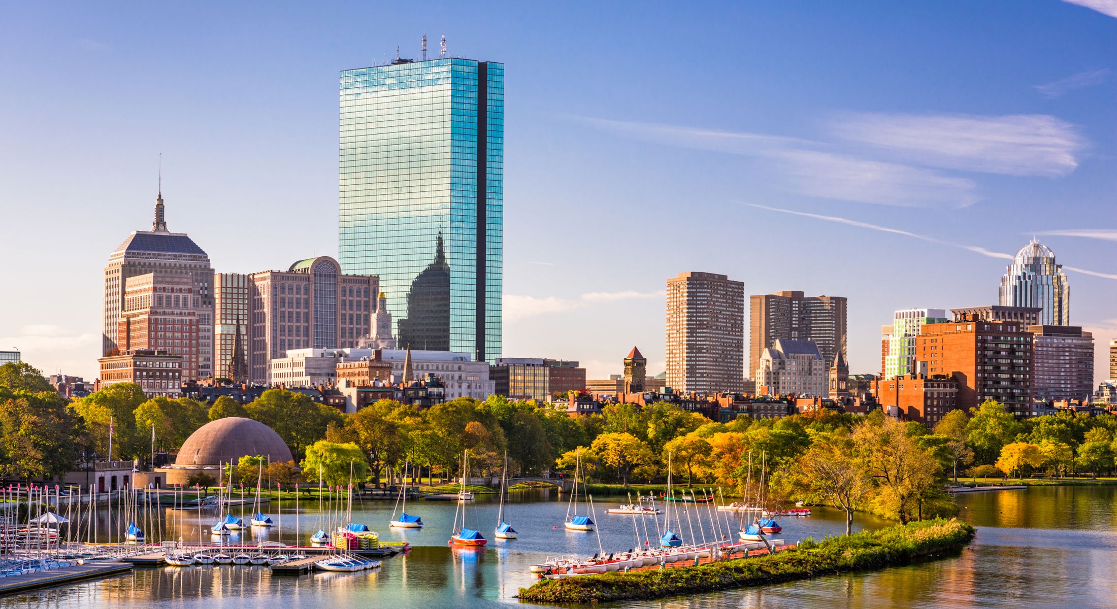 Boston skyline with parks and boats in water.